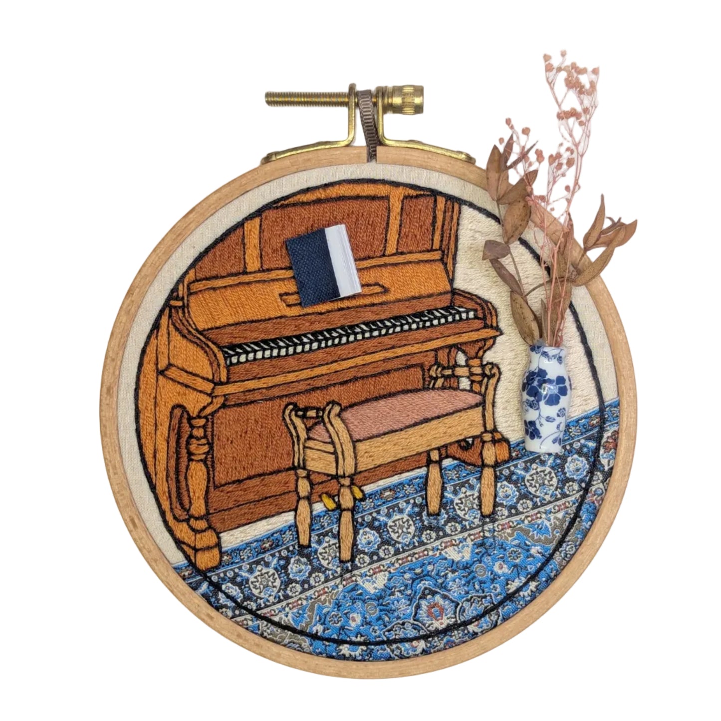 Embroidery hoop with a wooden piano on a blue patterned rug, on a white background