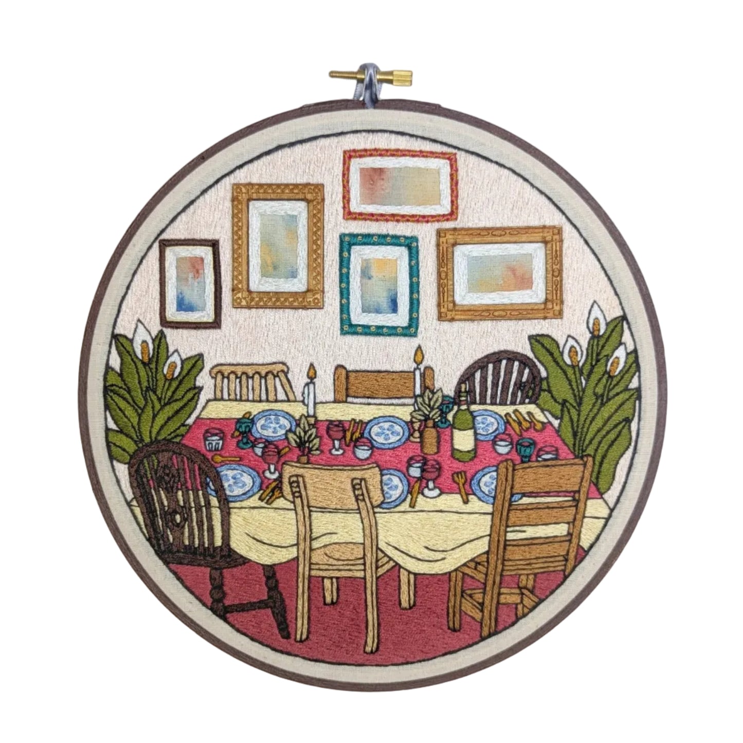 Embroidery hoop with a colorful depiction of a dining table and chairs, framed by pictures on a white background.
