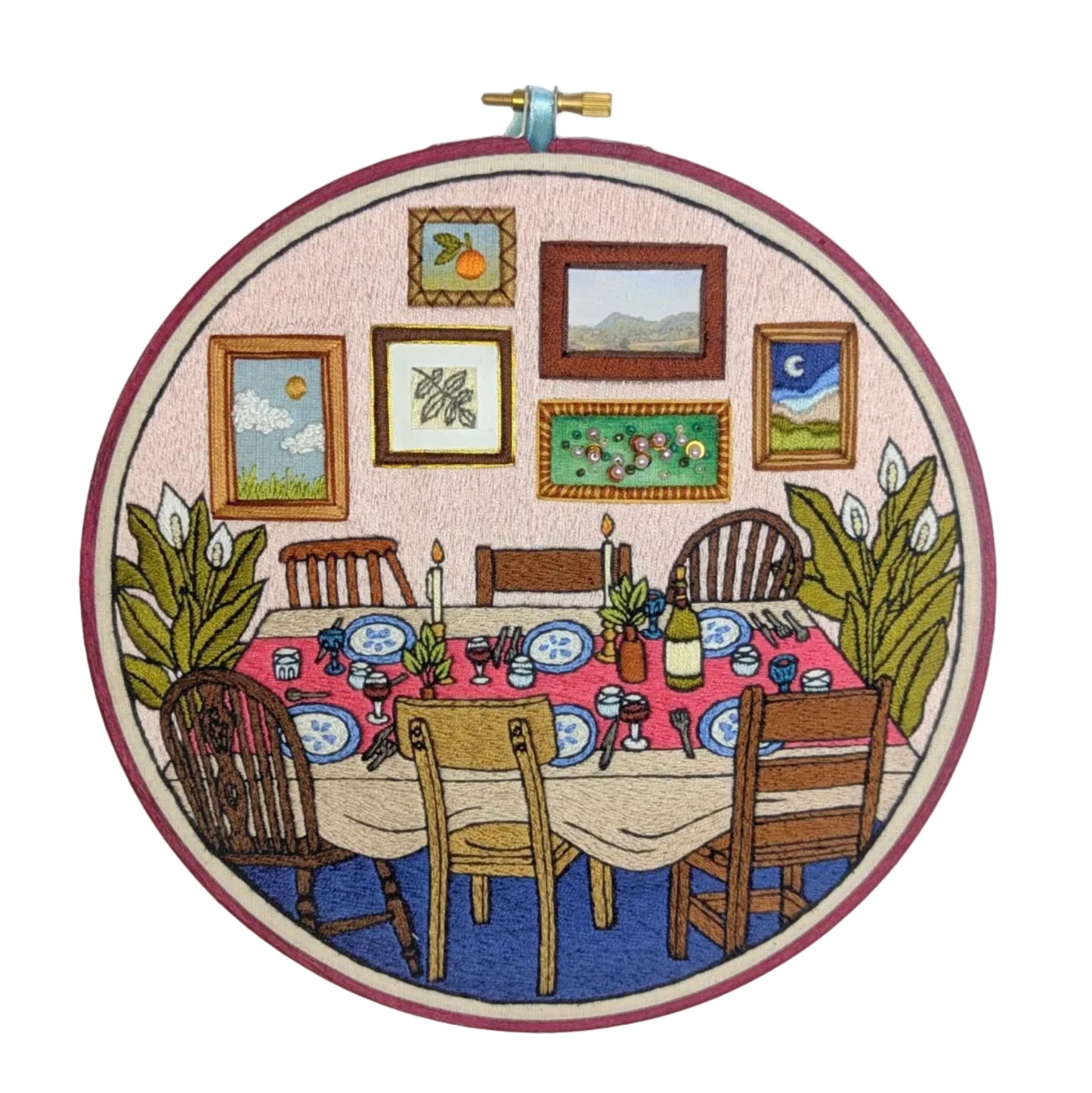 Embroidery hoop with a dining scene including a table, chairs, and wall art.