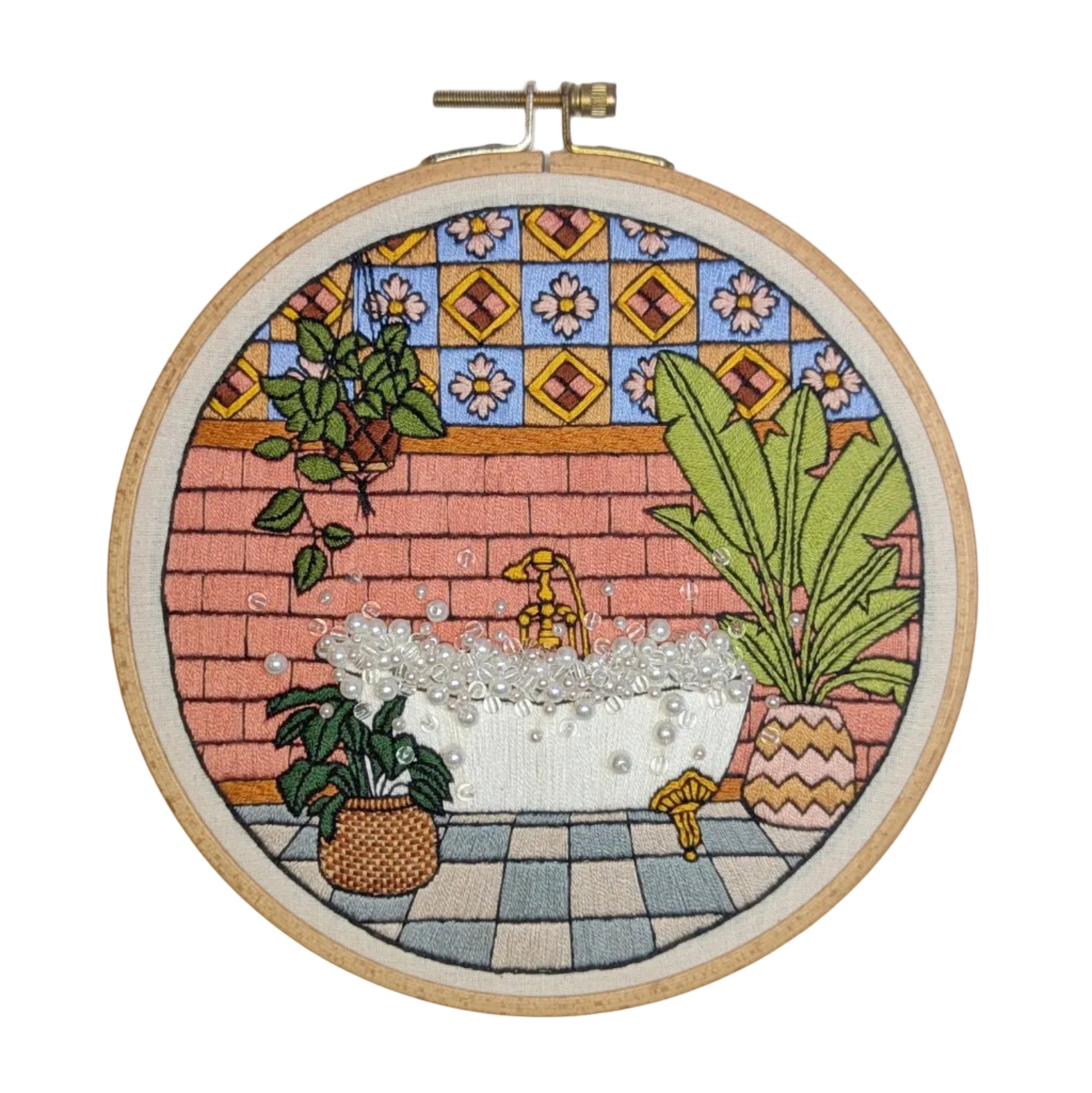 Embroidery hoop with a colorful stitched scene of a bathtub and plants on a tiled background