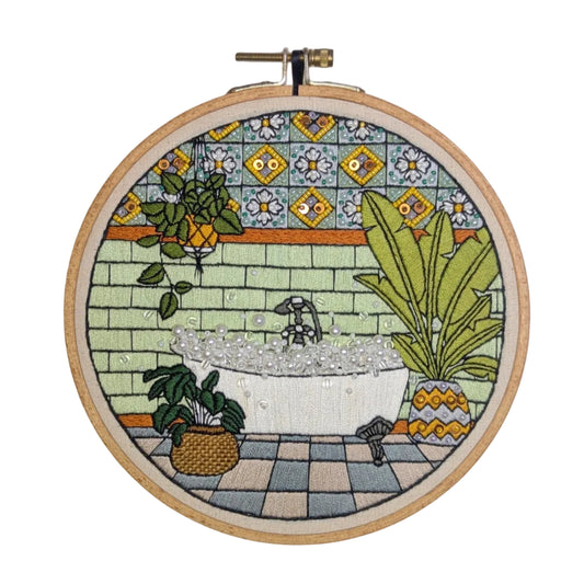 Embroidery hoop with a colorful depiction of a bathroom scene on a tiled background
