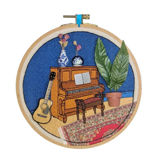 Embroidery hoop with a scene of a piano, guitar, and plants on a blue background