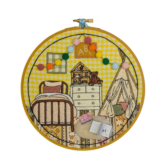 Embroidery hoop with a colorful children's room illustration on a yellow checkered background.
