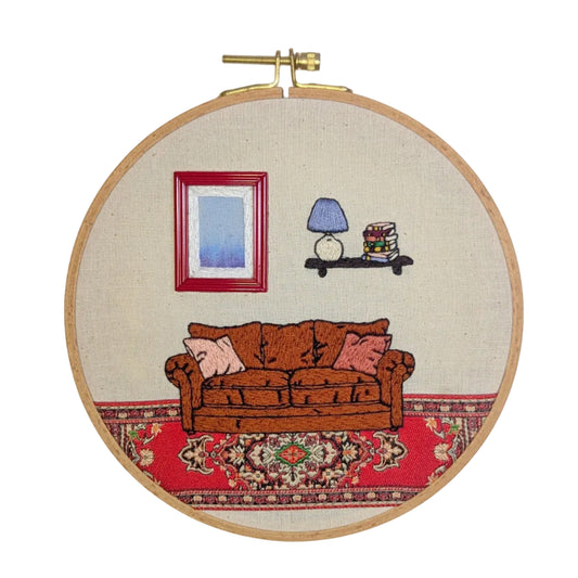 Embroidery hoop with a living room scene including a couch, lamp, and picture frame.